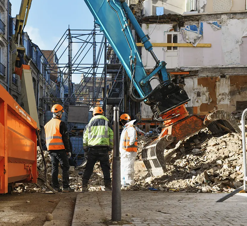Work crew using heavy machinery to remove the demolished remains of a large apartment building in a metropolitan area.
